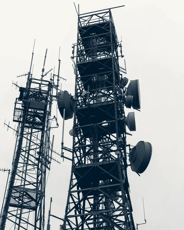 Dos torres de telecomunicaciones con antenas y parábolas bajo un cielo nublado